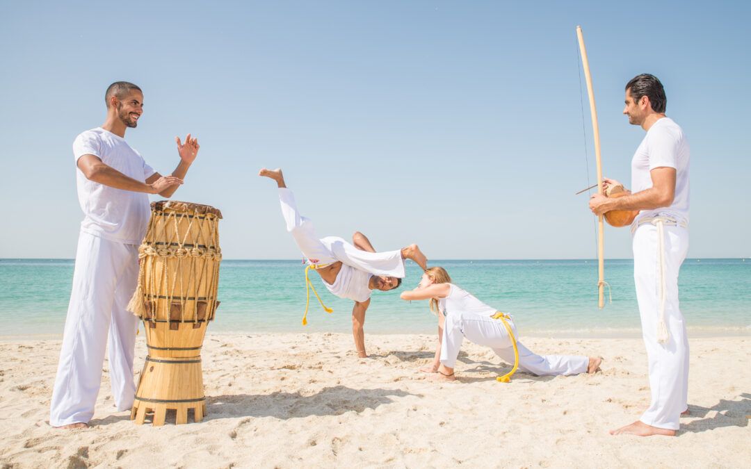 Grupo practicando capoeira en la playa acompañado de música tradicional.
