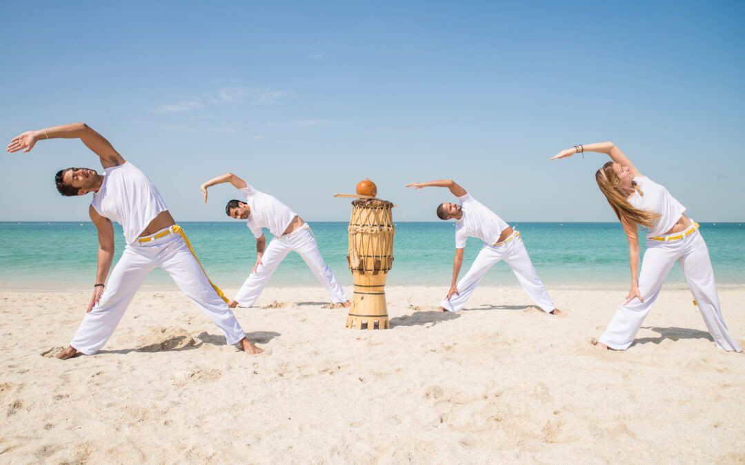Grupo realizando un calentamiento de capoeira en la playa al amanecer.