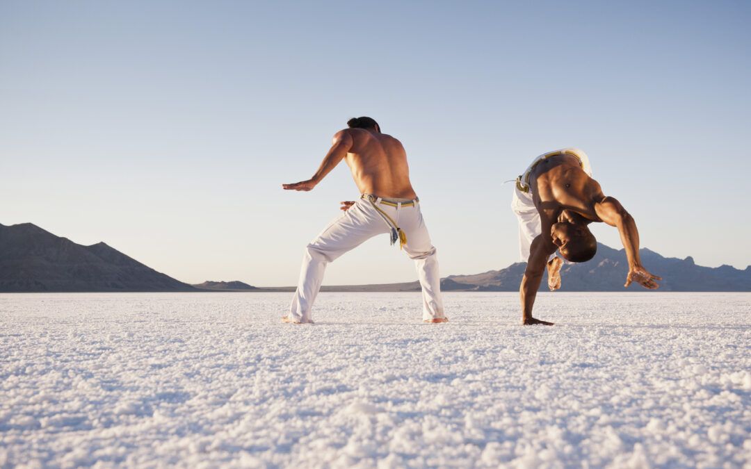 Capoeirista realizando una pirueta acrobática durante un combate en la playa.
